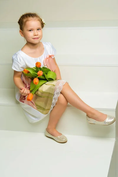 A little girl with a bouquet of tulips is sitting on the stairs. — Stock Photo, Image