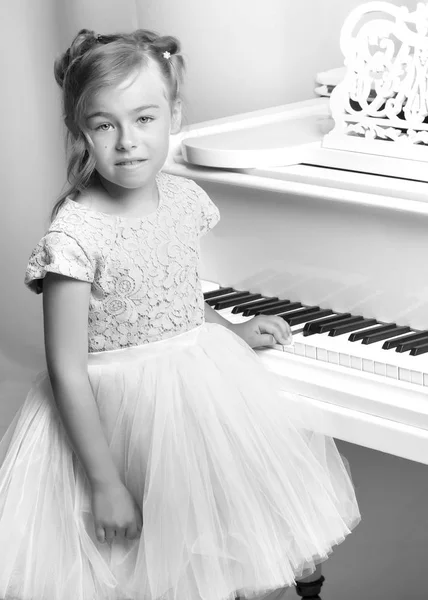 Menina bonita está tocando em um piano de cauda branco. — Fotografia de Stock