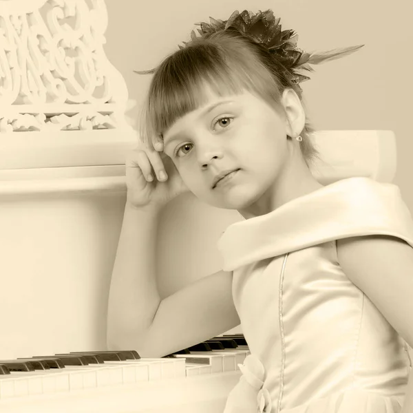 Uma menina está posando perto de um piano de cauda branco . — Fotografia de Stock