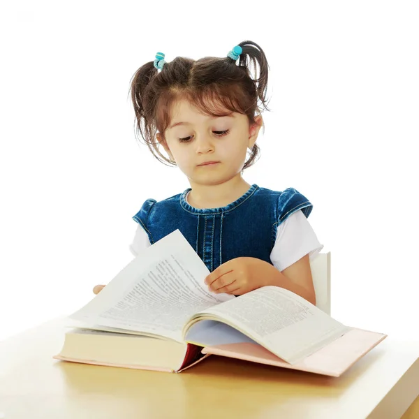 Маленька дівчинка читає книгу за столом . — стокове фото