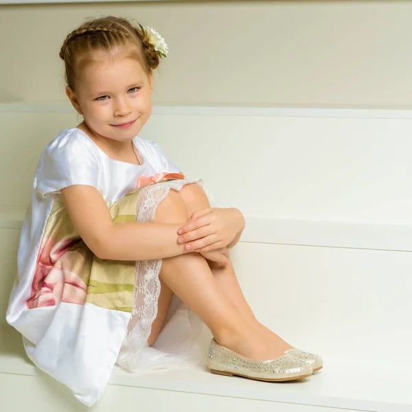 Mooi klein meisje zit op de witte trap. — Stockfoto