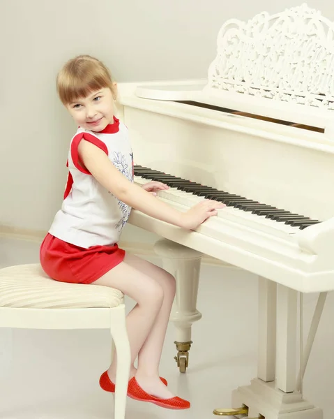 Beautiful little girl is playing on a white grand piano.