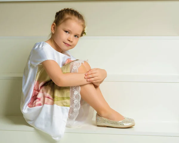 Beautiful little girl is sitting on the white staircase. — Stock Photo, Image