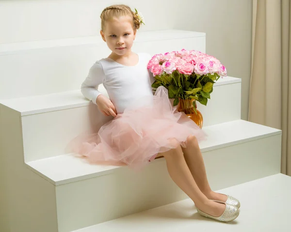 Meisje met een boeket bloemen zit op een witte trap. — Stockfoto