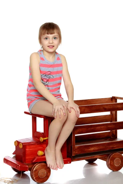 The girl is sitting on a large toy wooden car. — Stock Photo, Image