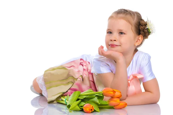 Une petite fille est allongée sur le sol avec un bouquet de tulipes . — Photo