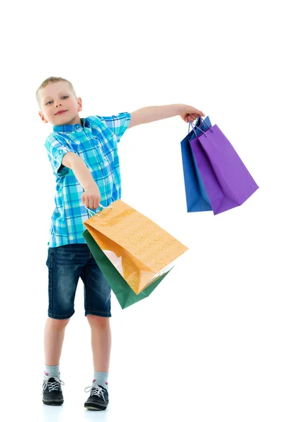 Маленький мальчик размахивает разноцветными бумажными пакетами. Он ходит по магазинам — стоковое фото