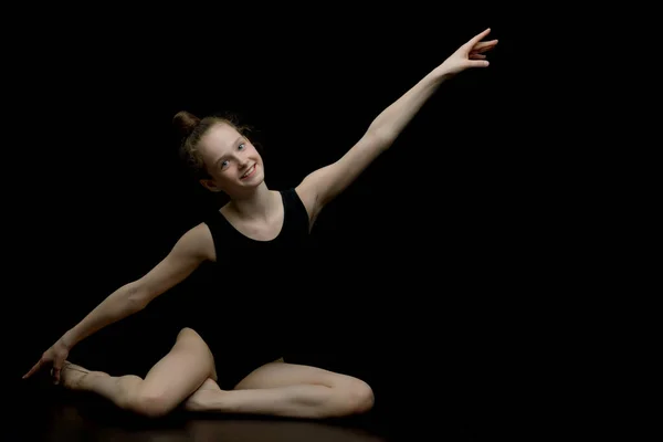 Chica gimnasta en el estudio sobre un fondo negro realiza gimnasias — Foto de Stock