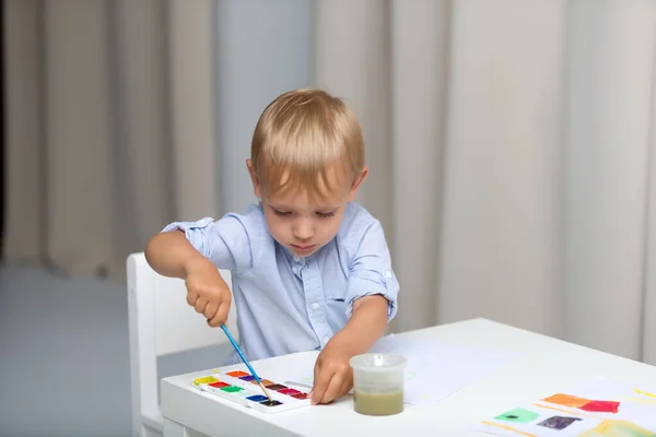 Mignon petit garçon peint à l'aquarelle tout en étant assis à la languette — Photo