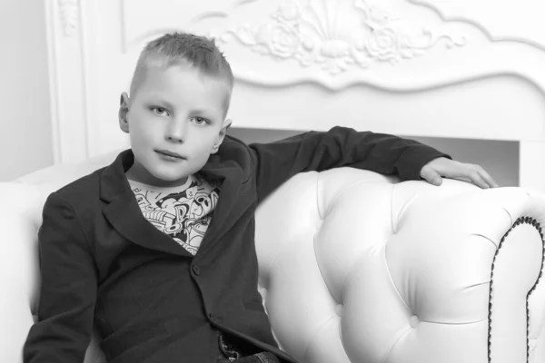 Un niño pequeño está sentado en el estudio en un sofá blanco. El cono —  Fotos de Stock