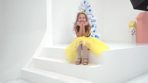 Kleines Mädchen sitzt auf einer weißen Treppe in der Nähe des Weihnachtsbaums — Stockvideo