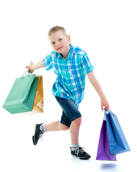 Lille dreng vinker flerfarvede papirsposer. Han går på indkøb - Stock-foto