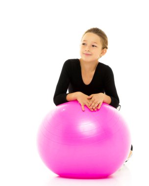 Küçük kız spor yapmak için büyük bir top üzerinde egzersiz yapıyor..