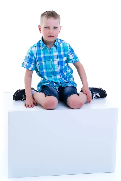 Een mooie kleine jongen wordt gefotografeerd in de buurt van een witte kubus. De co — Stockfoto