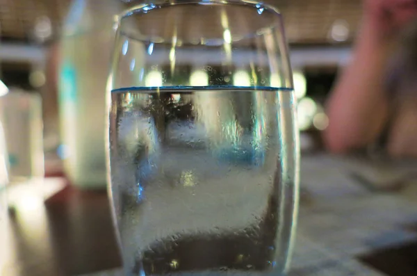 A misted glass of water stands on a table in a restaurant.