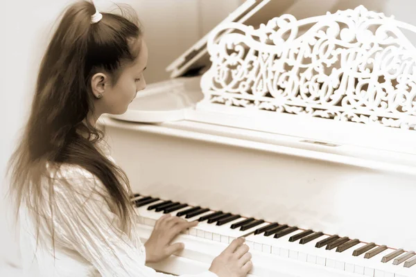 A teenage girl is playing on a white grand piano. — Stock Photo, Image
