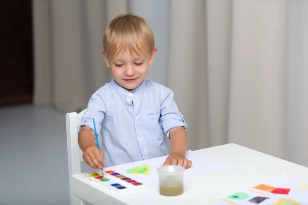 Cute little boy paints with watercolors while sitting at the tab — Stock Photo, Image