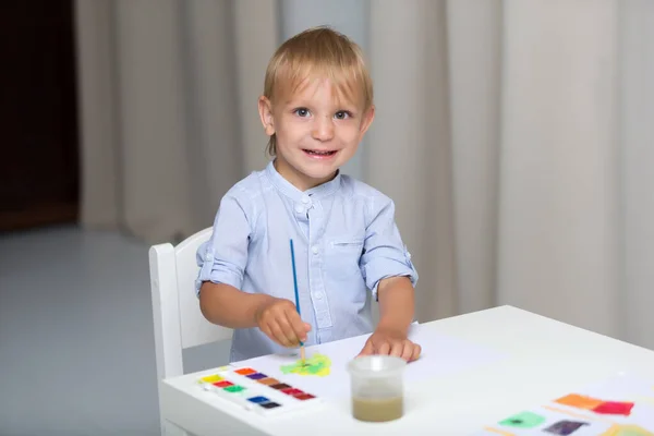 Söt liten pojke målar med akvareller medan du sitter på fliken — Stockfoto