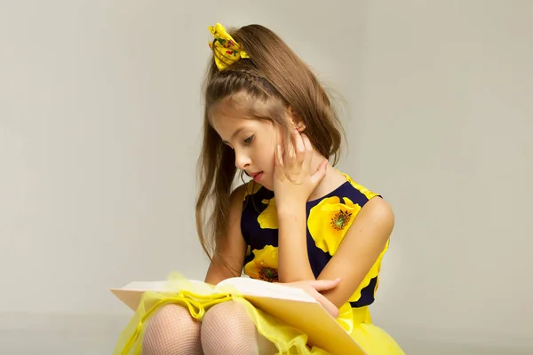 Little girl schoolgirl is sitting on the stairs and reading a bo — Stock Photo, Image