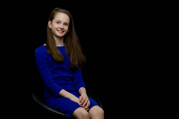 Stock image Charming girl teenager sitting on a chair in the studio on a bla