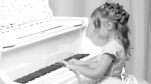 Beautiful little girl is playing on a white grand piano. — Stock Photo, Image