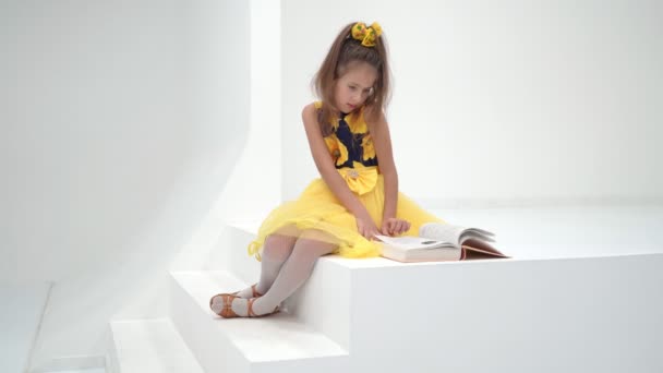 Little girl schoolgirl is sitting on the stairs and reading a bo — ストック動画