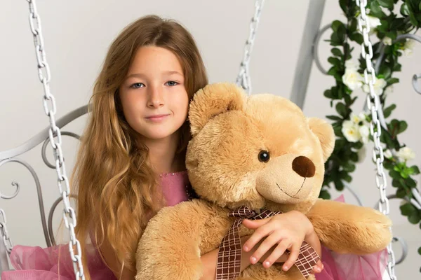 一个小女孩和泰迪熊在秋千上荡秋千. — 图库照片