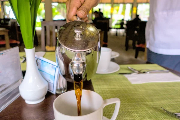 Mannen häller varmt kaffe från kaffekannan i den vita — Stockfoto