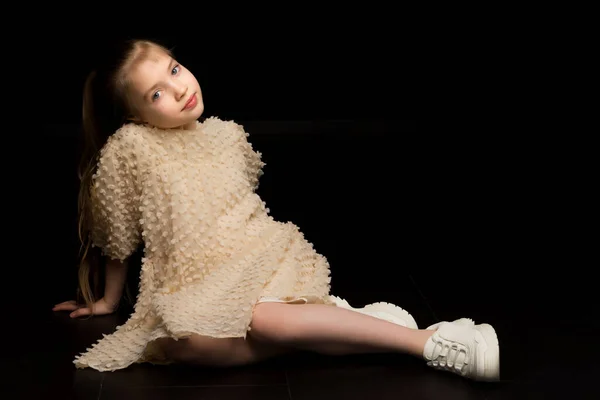 Ein kleines Mädchen sitzt im Studio auf dem Fußboden auf einem schwarzen B — Stockfoto