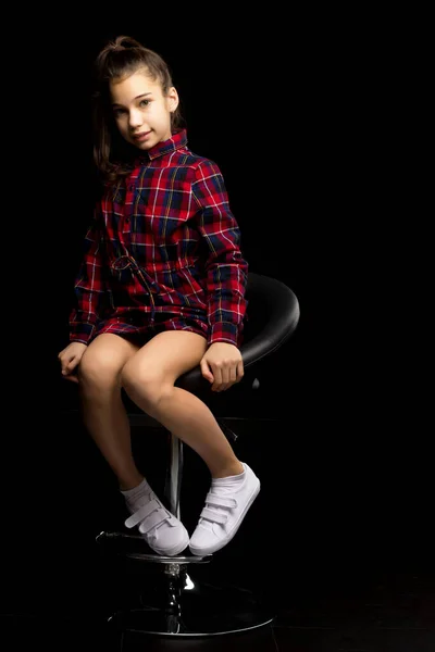 Chica encantadora adolescente sentada en una silla en el estudio en un bla —  Fotos de Stock