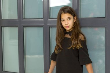 Küçük kız büyük bir panoramik pencerenin yanında poz veriyor.