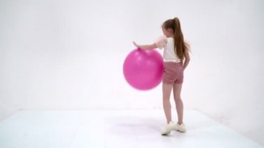 Küçük kız spor olsun diye büyük bir topla oynuyor.