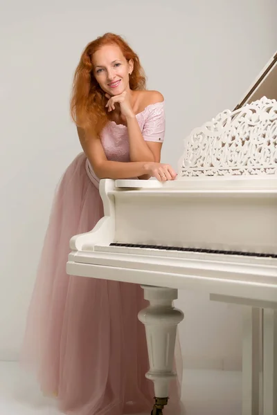 Mulher bonita perto de um piano de cauda branco . — Fotografia de Stock