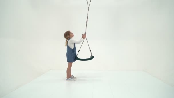 Mooi blond meisje swingen op touw schommel en kijken naar camera — Stockvideo