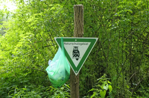 Waste in the nature reserve - warning sign Nature reserve to which a bag with garbage was hung