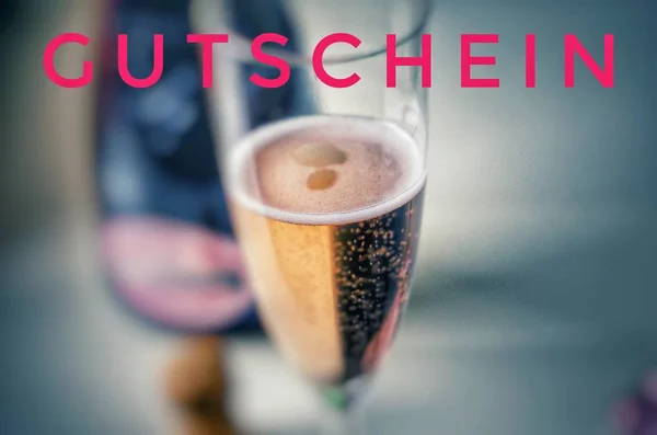 Champagne glass with noble champagne and inscription in pink on german Gutschein, in english coupon, voucher, gift card