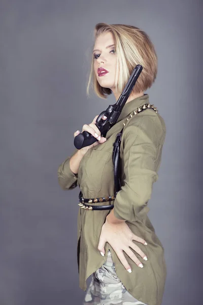 Retrato de niña adulta joven vestida con camisa de estilo militar y cinturón sosteniendo la pistola cerca del hombro —  Fotos de Stock