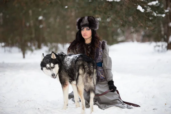 Menina adulta bonita sentada com cão husky na floresta de neve — Fotografia de Stock