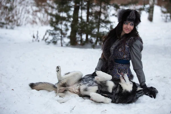 Atrakcyjna dziewczyna gra z psem husky, leżącego na śniegu — Zdjęcie stockowe