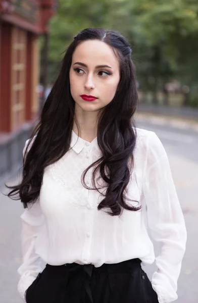 Портрет молодой брюнетки в белой блузке, стоящей на улице — стоковое фото