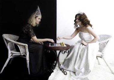 Kraliçe elbiseler, birbirimizi karşısında oturan ve satranç oynarken elmas taç giyen iki kız.