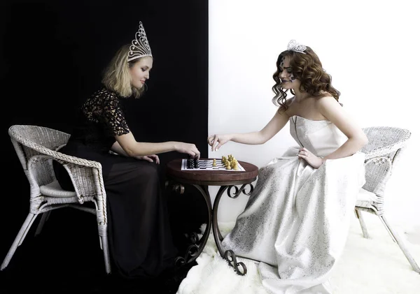 Two girls wearing queen dresses, diamond crown sitting opposite to each other and playing chess. — Stock Photo, Image