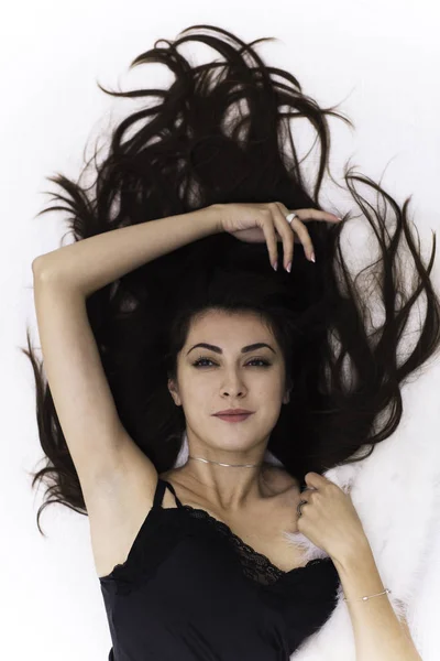 Portrait of the beautiful young brunette woman with long dark hair lying on white — Stock Photo, Image