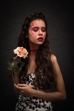 Gül çiçek tutan boyalı renkli yüz çekici genç esmer kadın portresi. Koyu arka plan.