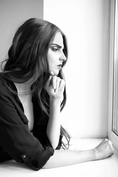 Indoors black and white portrait of attractive young woman wearing dark shirt looking to window