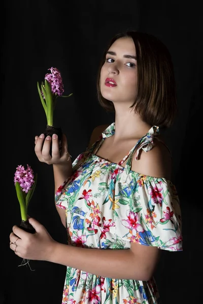 Красивая девушка наполовину поворачивается и держит два свежих рваных гиацинтовых цветов лампочками и глядя в камеру — стоковое фото