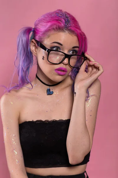 Portrait of young attractive woman with heavy makeup in black top and heart-shaped choker. Holding her black eyeglasses in hand and looking away. — Stock Photo, Image