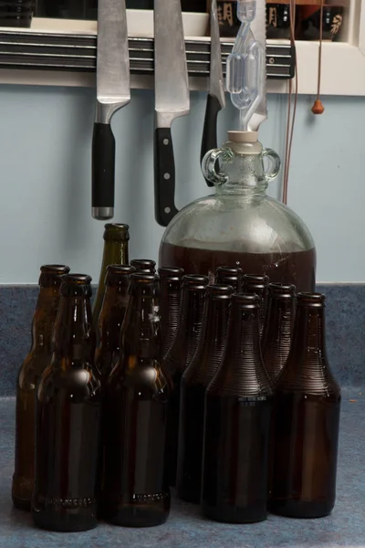 Που έχουν υποστεί ζύμωση μπύρας μια νταμιτζάνα με αεροφράκτη και καφετιά μπουκάλια και μαχαίρια κουζίνας φόντο — Φωτογραφία Αρχείου