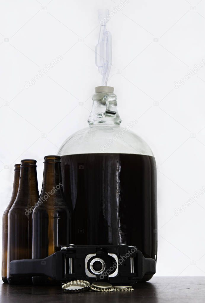 Fermented beer in a demijohn with airlock and brown bottles and over light background