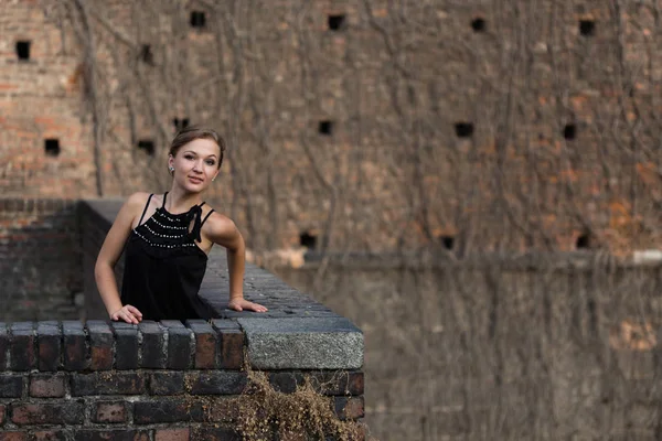 Schönes Mädchen in schwarzem Kleid steht über alter Backsteinmauer — Stockfoto